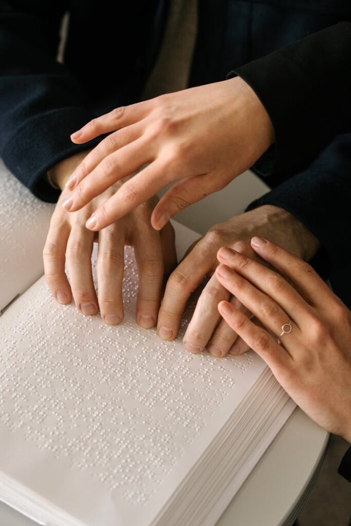 Close-up of hands reading a braille book, emphasizing touch and assistance.